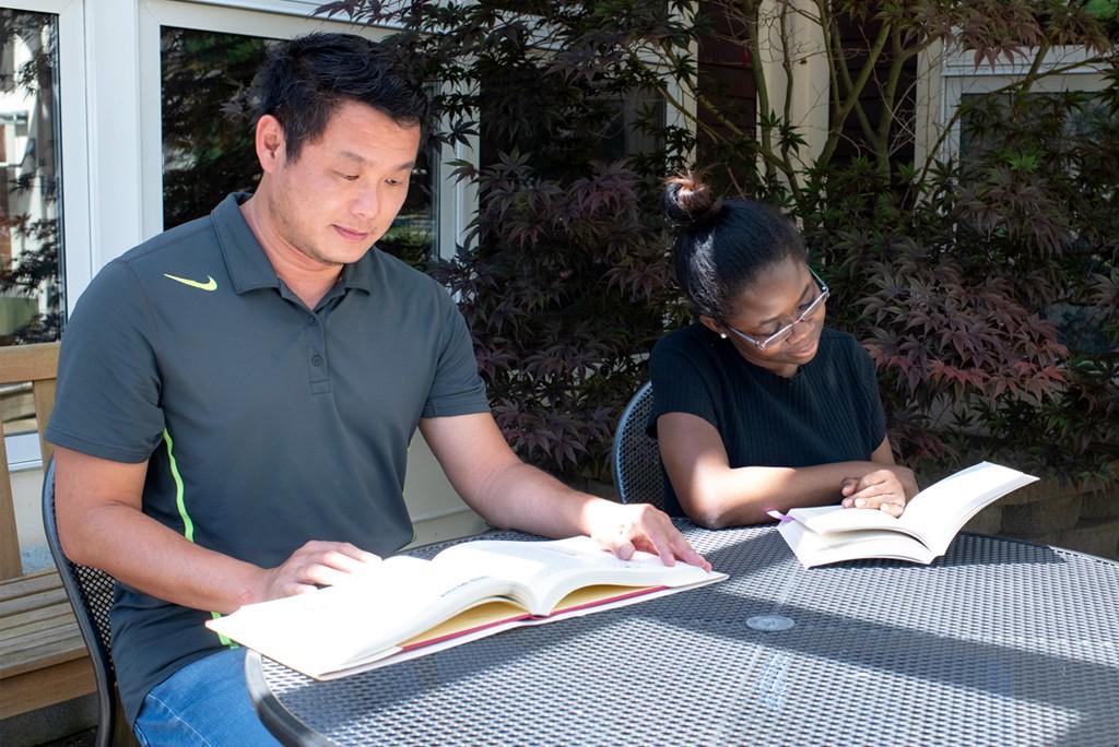 两个联合国学生坐在外面的一张桌子旁，每人读一本教科书