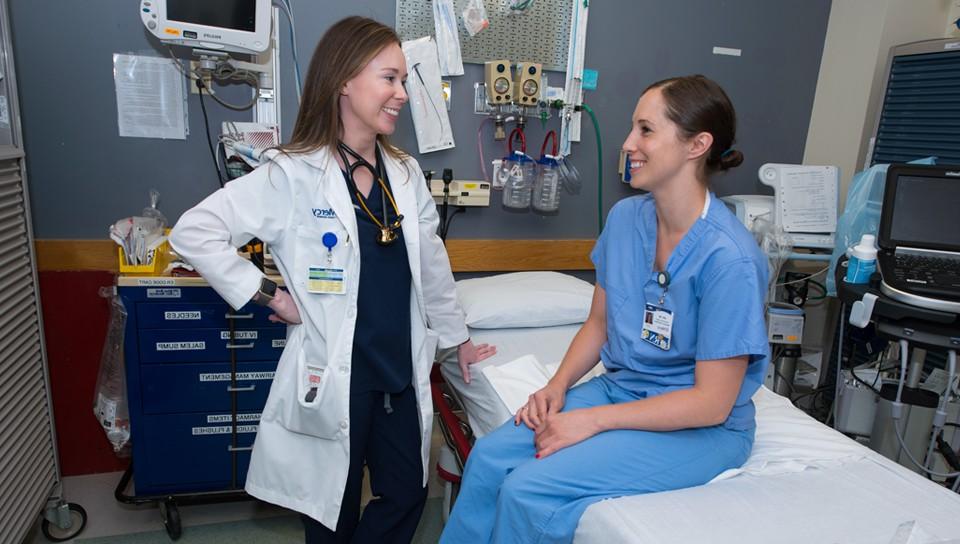 U N E Physician Assistant student in a white coat talks to a patient in a hospital room