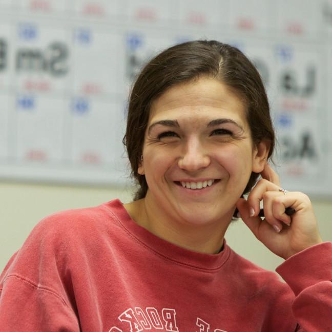 a student smiles in front of a poster of the periodic table