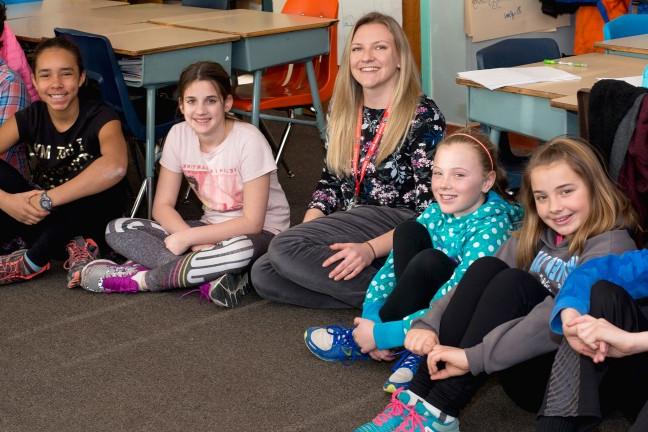 A teacher sits on the floor with her young students